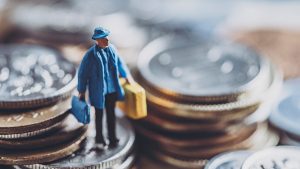 Miniaturade empresário sobre pilhas de moedas. Foto: Adobe Stock