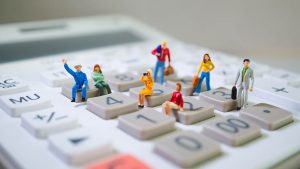 Pessoas em miniatura sentadas sobre as teclas de uma calculadora