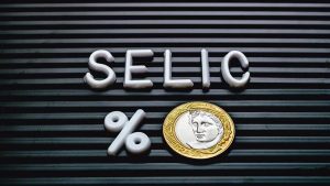 Palavra Selic em cima de um sinal de porcentagem e moeda de R$ 1. Foto: Adobe Stock