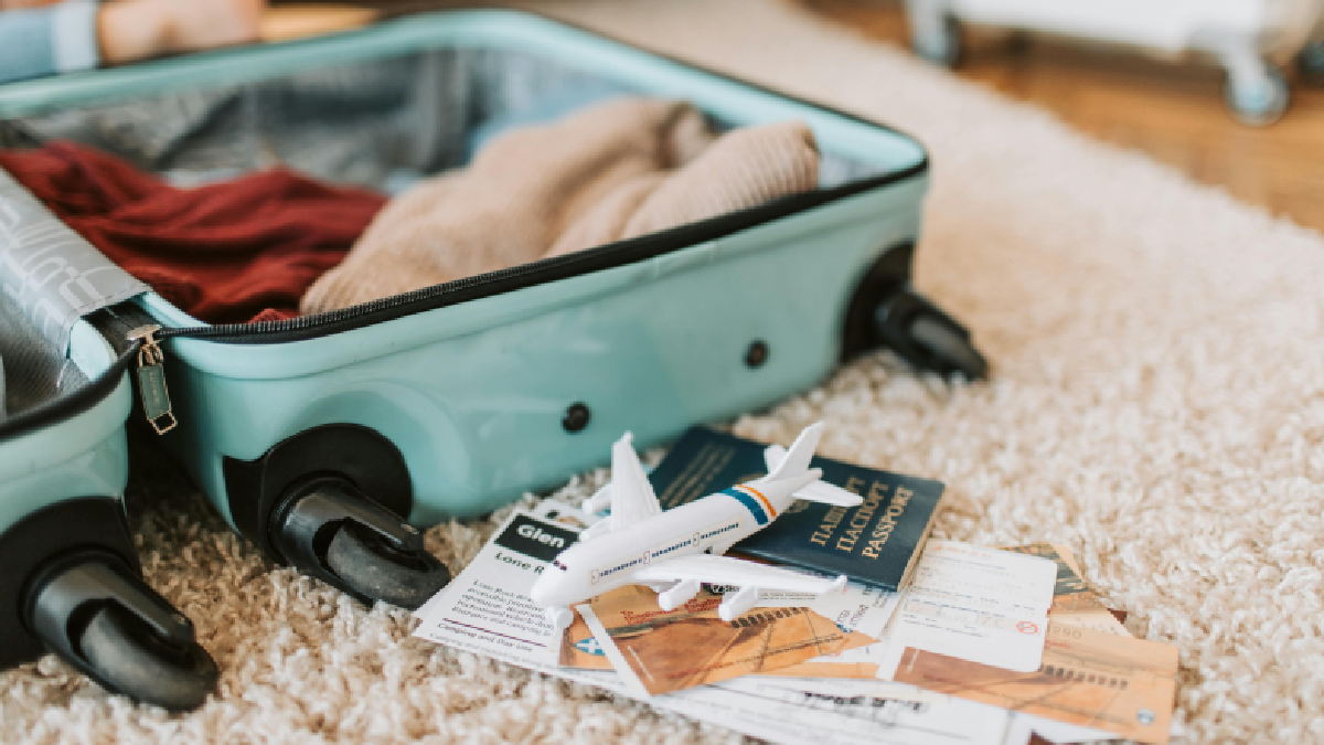 Mala aberta, passagens, passaporte e miniatura de avião em cima de tapete. Foto: Pexels