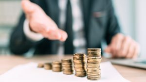 Empresário com a mão estendida e pilha de moedas (Fonte: Adobe Stock)