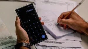 Calculadora em telefone e mão escrevendo contas. Foto: Joédson Alves/Agência Brasil