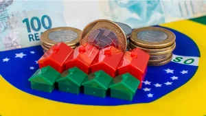 miniatura de casas e moeda de real. Foto: Adobe Stock