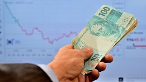 Mão segurando notas de cem reais